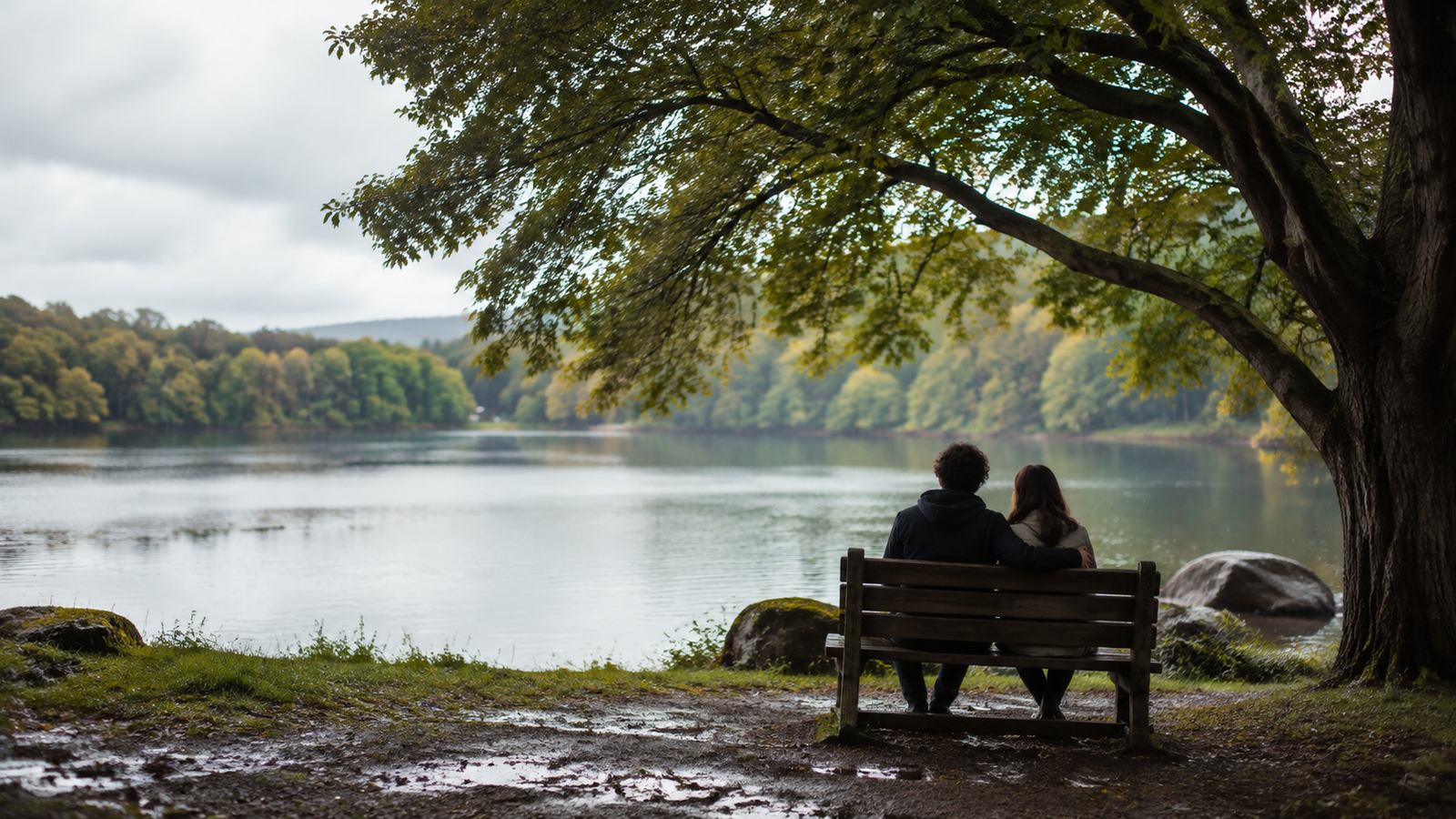 Dos personas permanecen juntas en silencio frente a un lago después de la lluvia